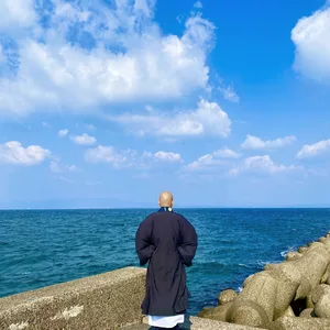 防波堤から海を見つめる僧侶の後ろ姿
